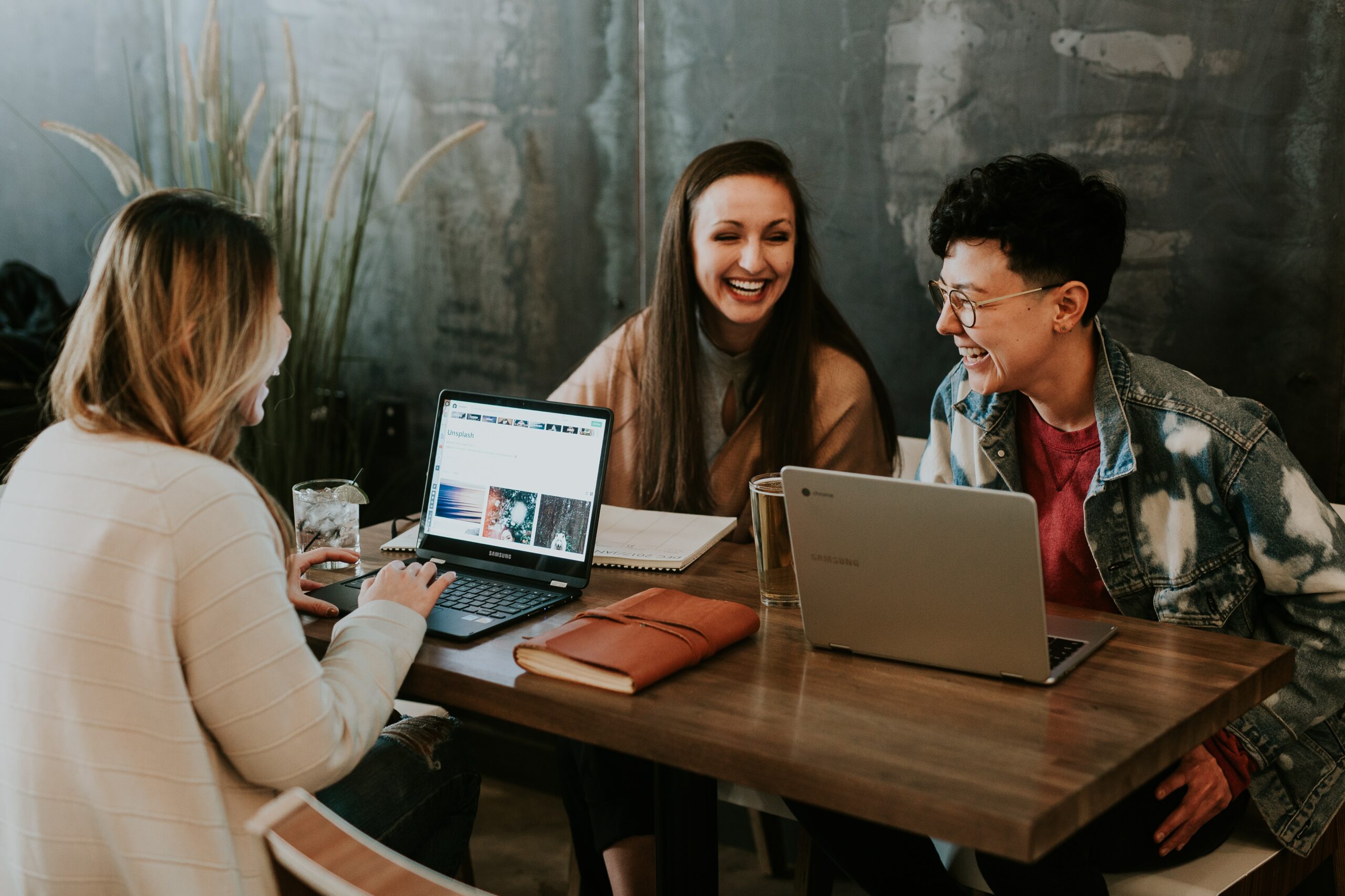 3 coworkers sitting at a wooden desk with laptops, smiling