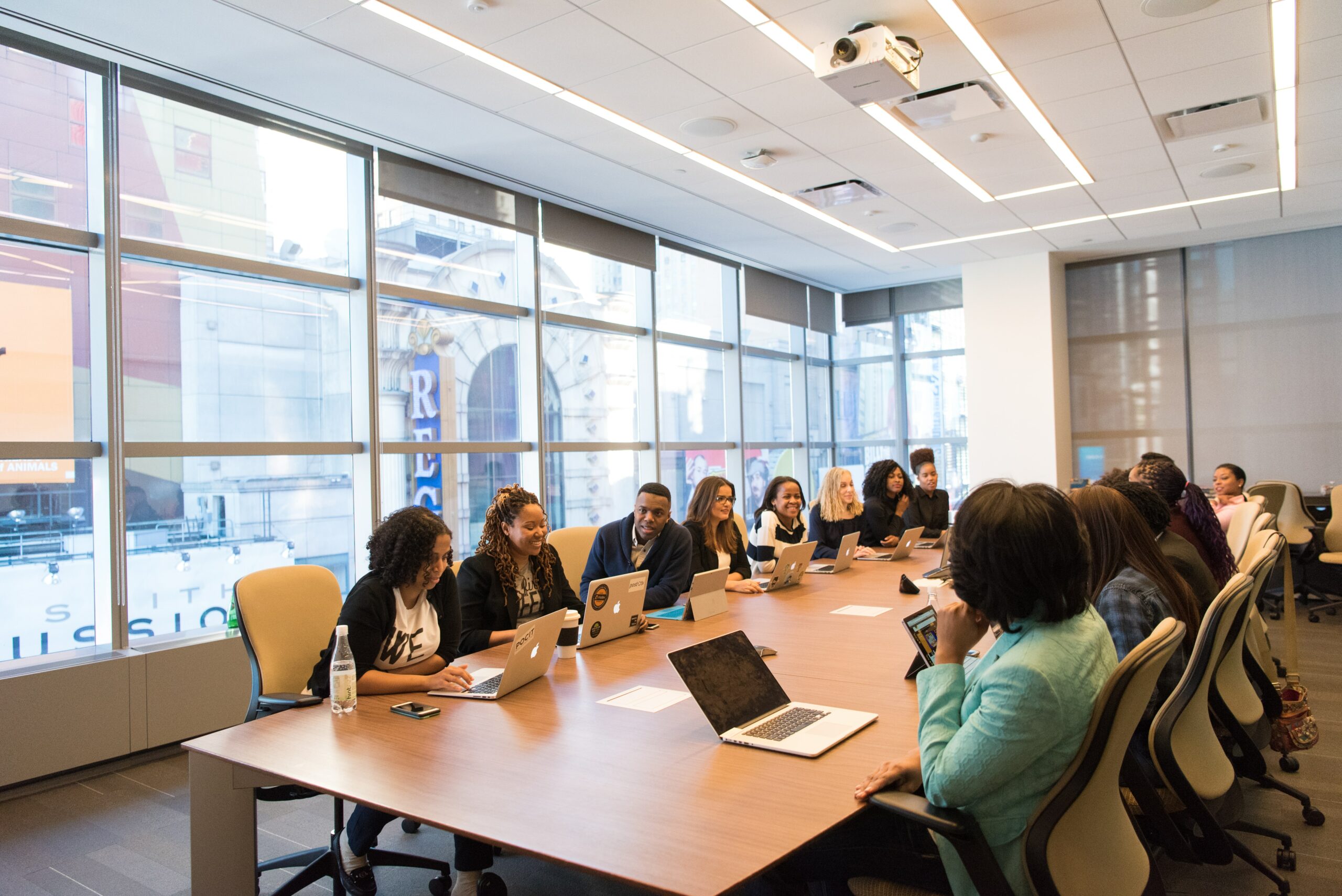 Coworkers seated around a long wooden conference table in a windowed conference room