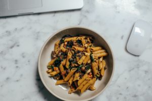 Plate of pasta next to a laptop and mouse